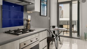 Een moderne keuken met een gasfornuis, een blauwe achterwand en een eethoek met een tafel en stoelen.