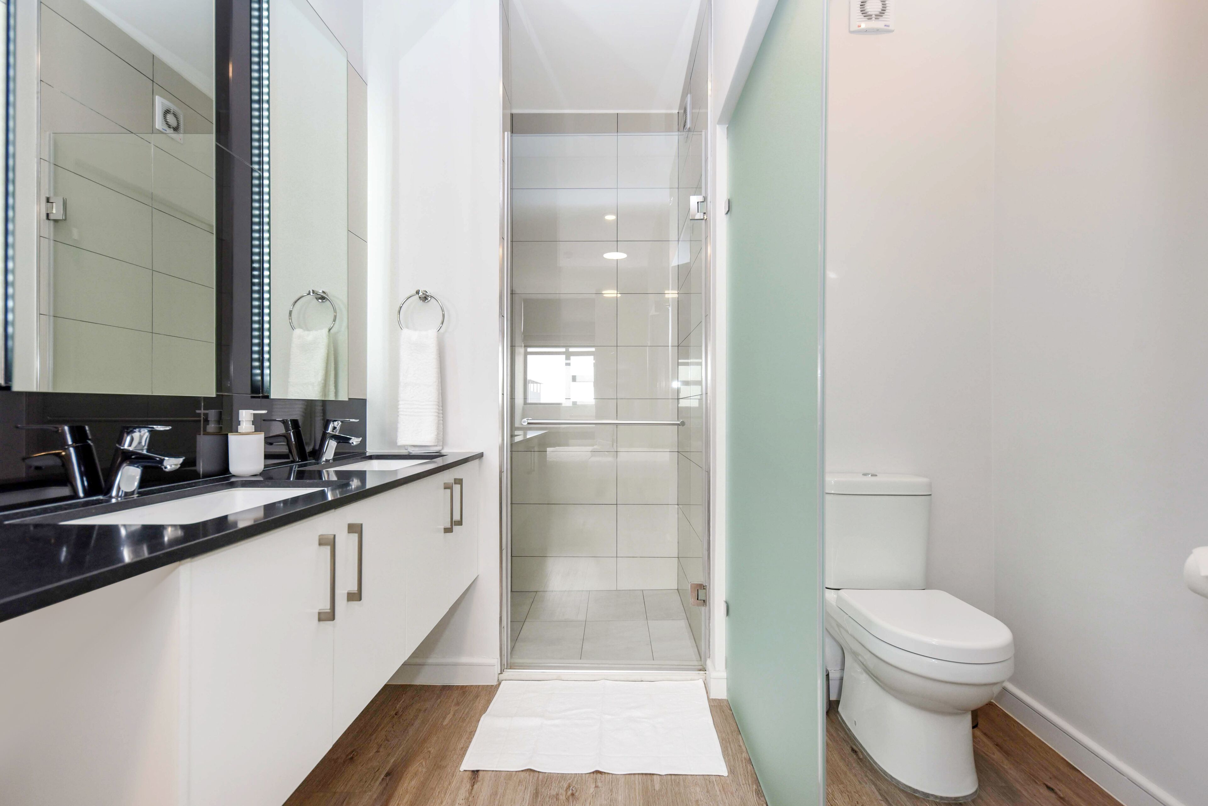 A modern bathroom with a glass shower enclosure, a white toilet, and a black countertop with a mirror.