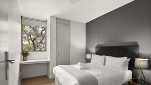 Een moderne slaapkamer met een groot bed, een raam met uitzicht, een nachtkastje en een lamp.