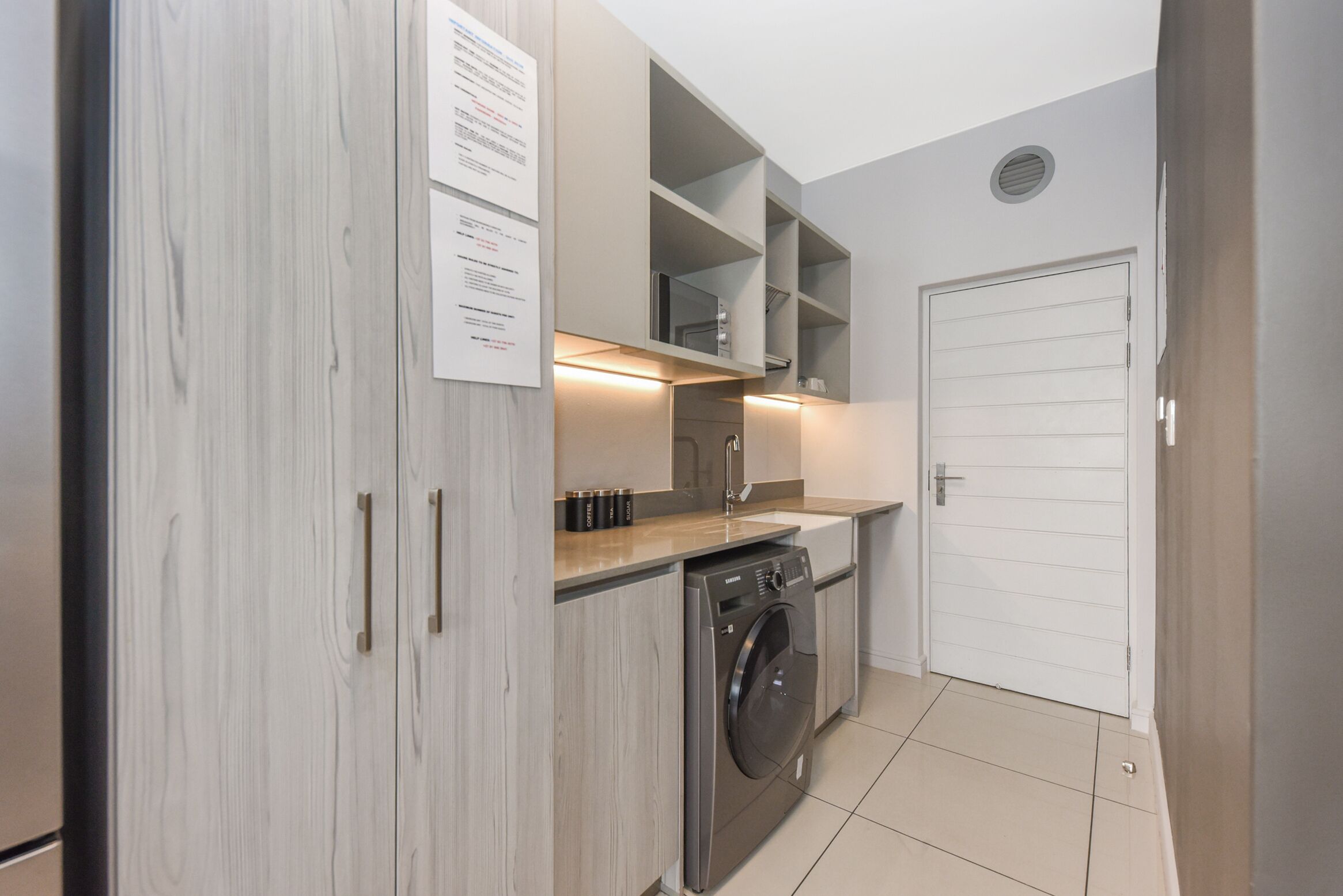 Cocina compacta con lavadora, estantes empotrados y una puerta blanca.