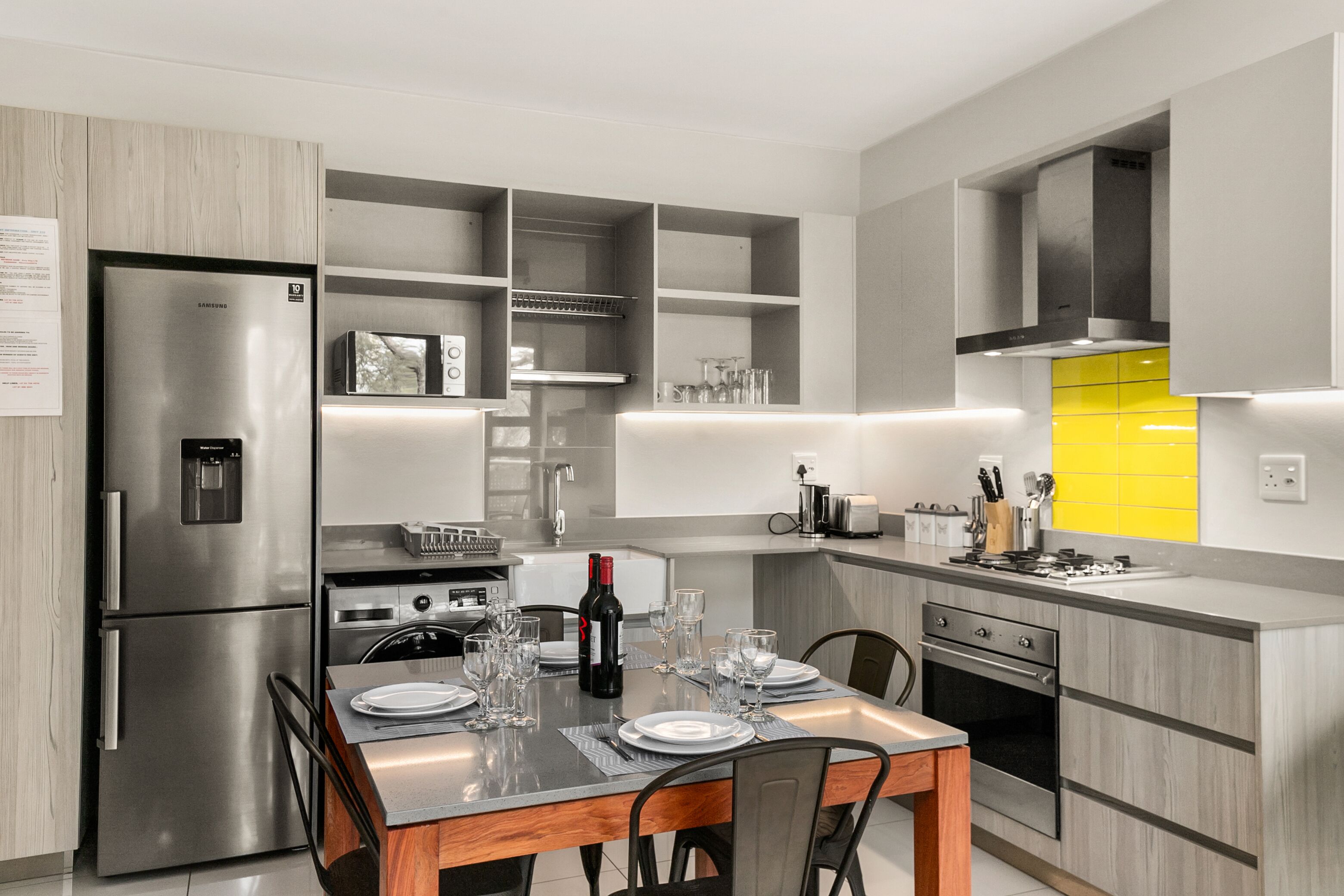 A modern kitchen with built-in appliances, a dining table set for four, and a yellow accent wall.