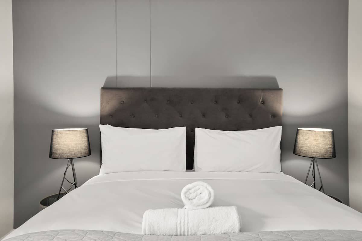 A hotel room with a large bed, two bedside lamps, a neatly folded towel, and a grey headboard.