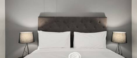 Ett hotellrum med en stor säng, två sänglampor, en prydligt vikt handduk och en grå sänggavel.
