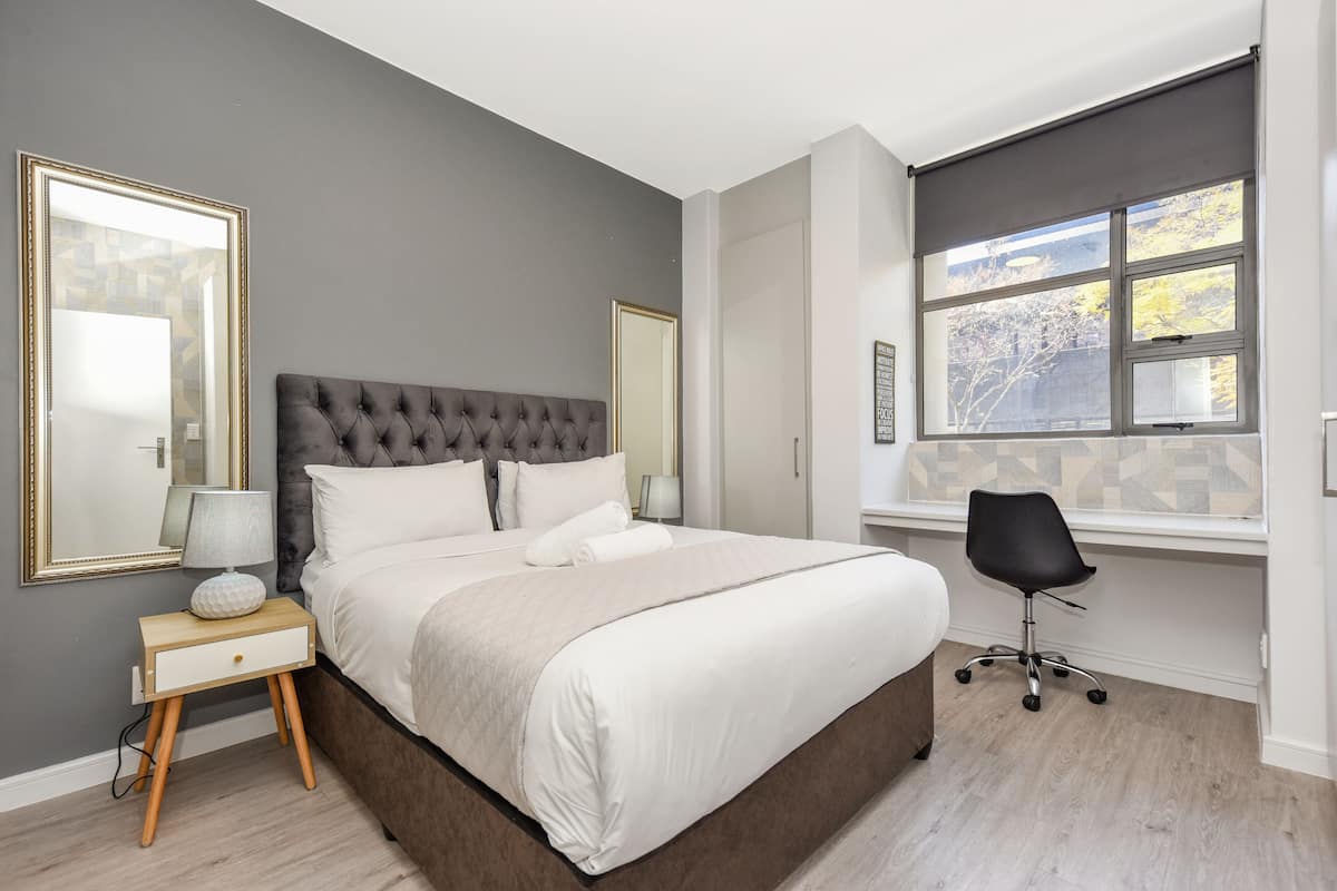 A modern bedroom with a large bed, bedside tables, a chair, and a window with a view.