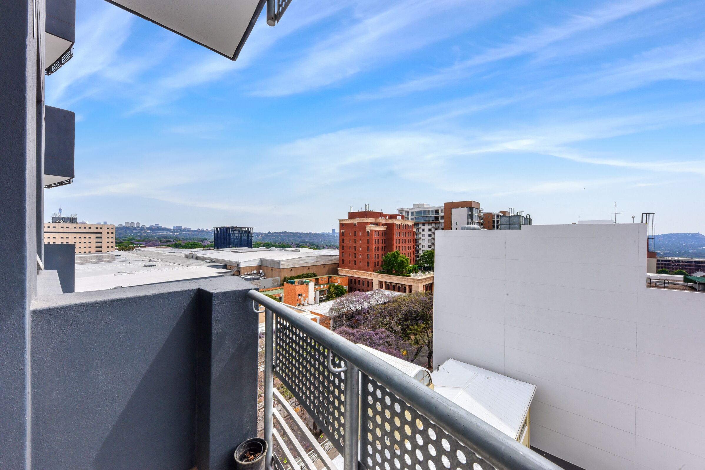 Un balcón con vistas a un paisaje urbano, incluyendo varios edificios y un cielo despejado.