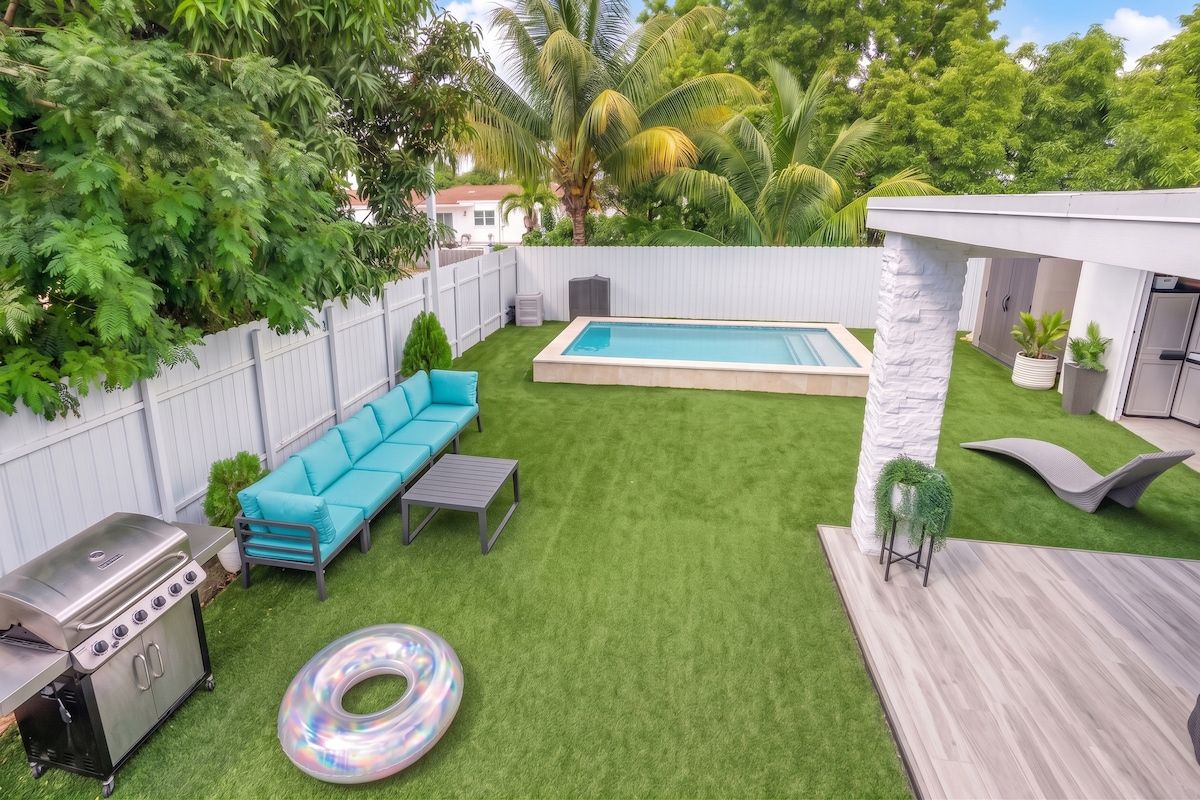 Un jardin avec une piscine, un canapé bleu, un barbecue et une terrasse en bois.