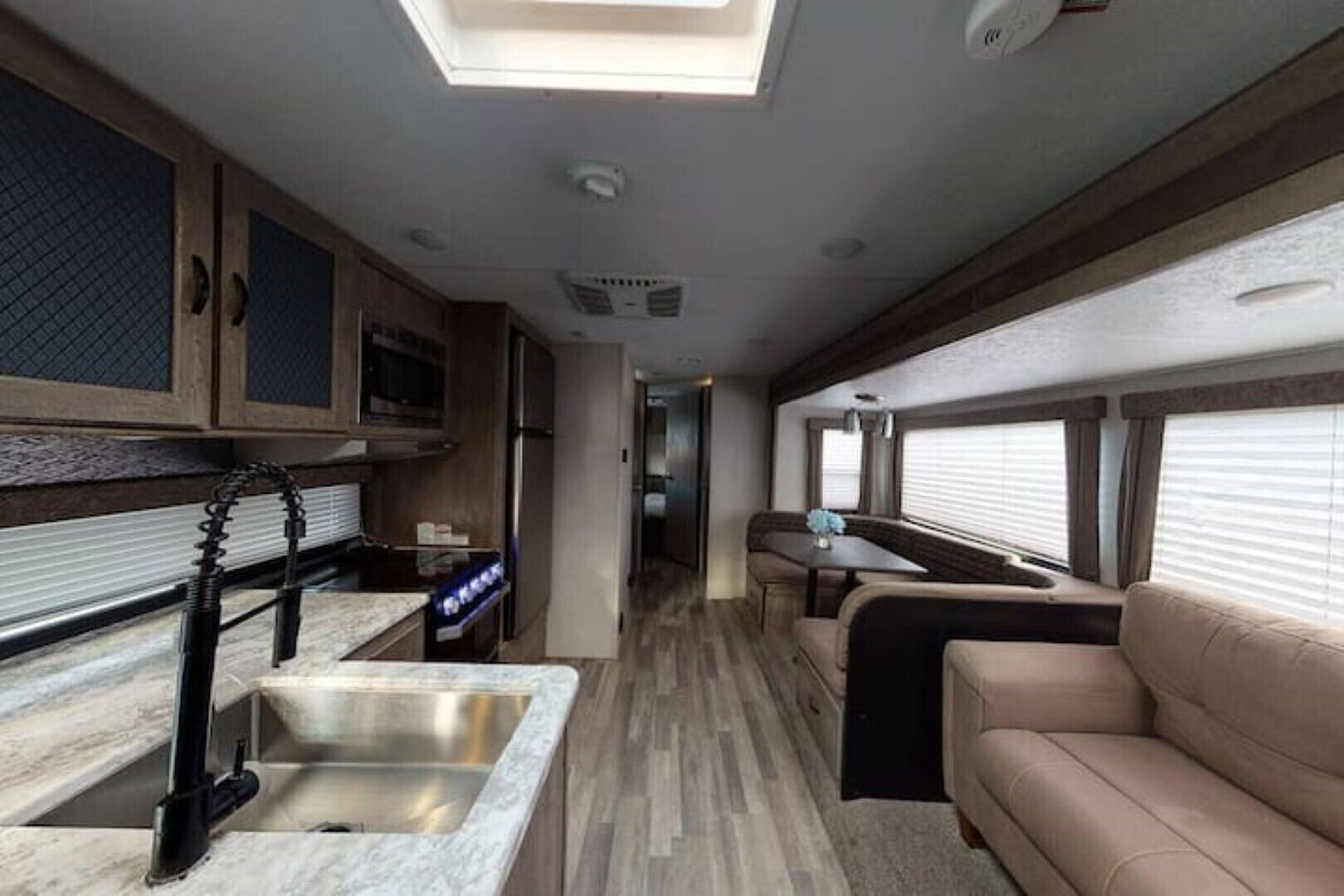 A compact RV interior with a kitchenette, a dining area, and a seating space.