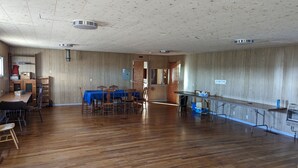 Tilava huone, jossa on puulattiat, ruokapöytä tuoleineen, baarialue ja puuseinä, johon on kiinnitetty kyltti, jossa lukee: »LOCK GHAIT I MADE».