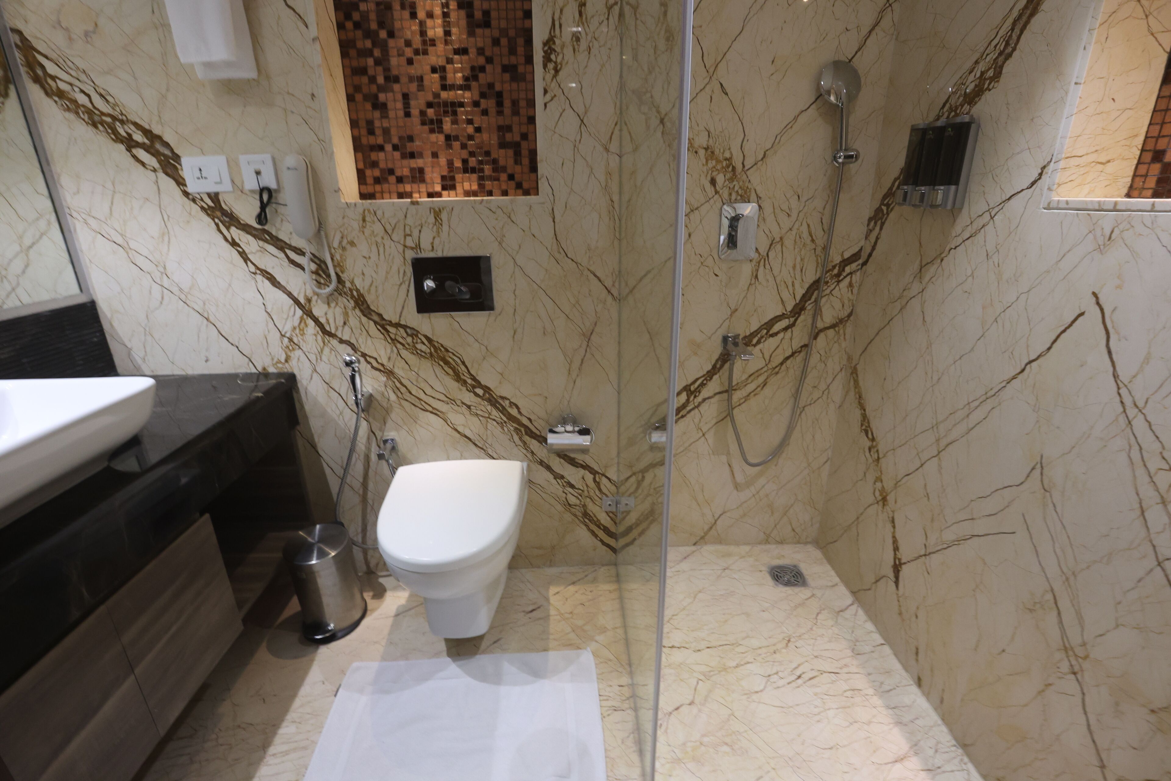 A modern bathroom with a glass-enclosed shower, a white toilet, and a marble wall with a decorative tile backsplash.