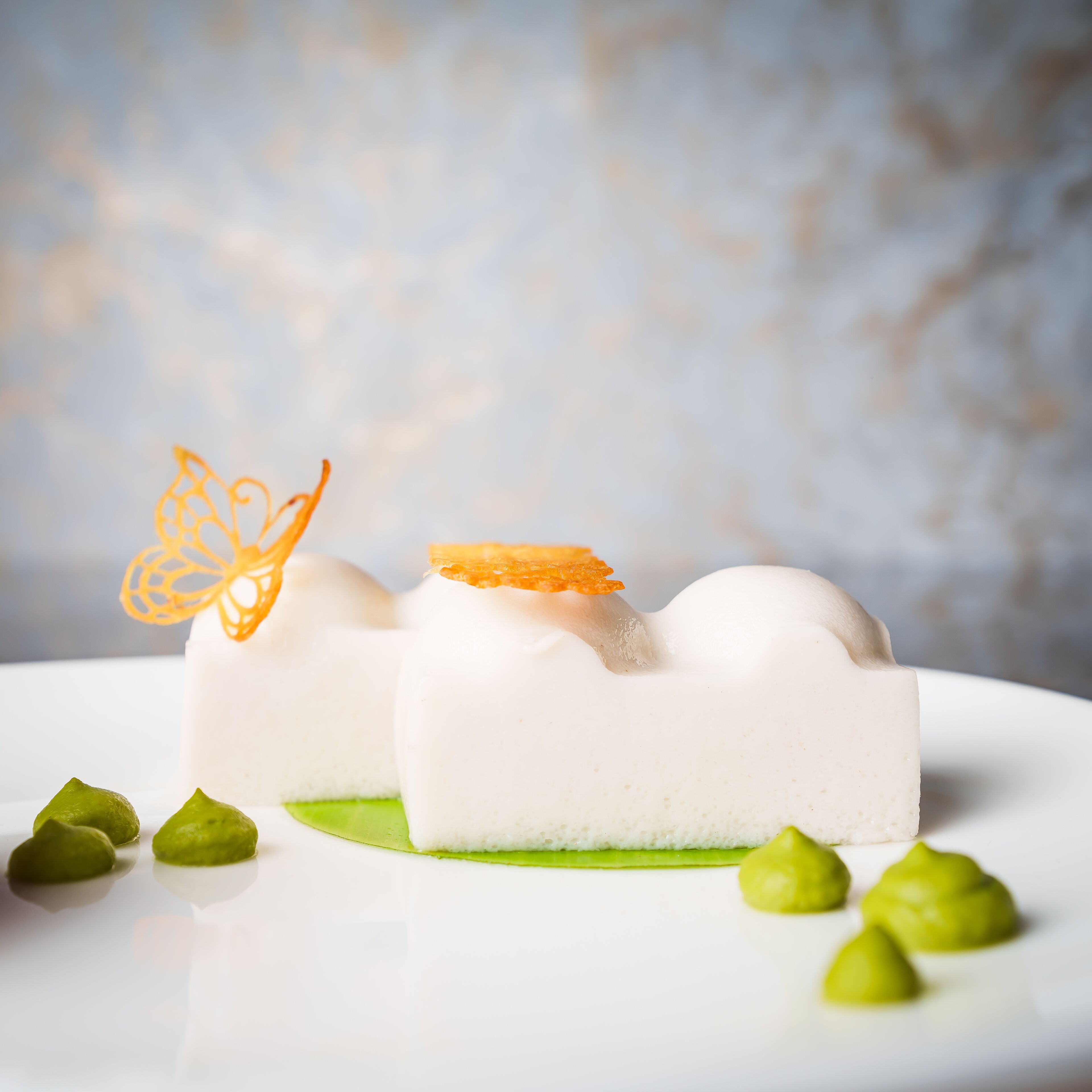 Un postre sobre una base blanca y decoración verde, sobre un plato blanco.