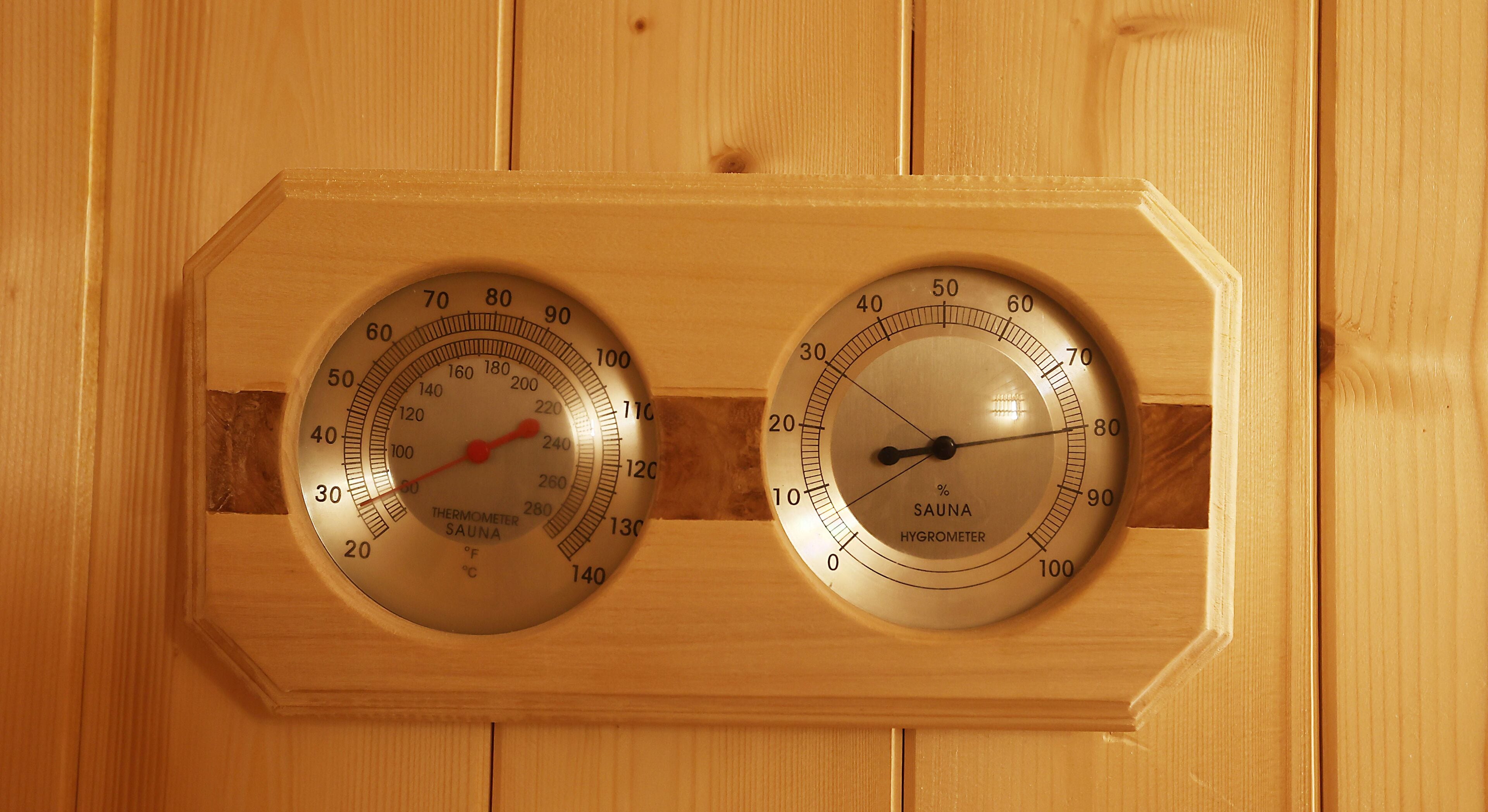 Two wooden wall-mounted gauges, one for temperature and one for humidity, in a sauna setting.