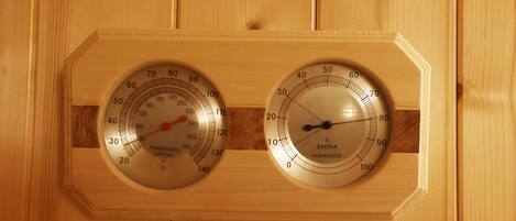 Two wooden wall-mounted gauges, one for temperature and one for humidity, in a sauna setting.