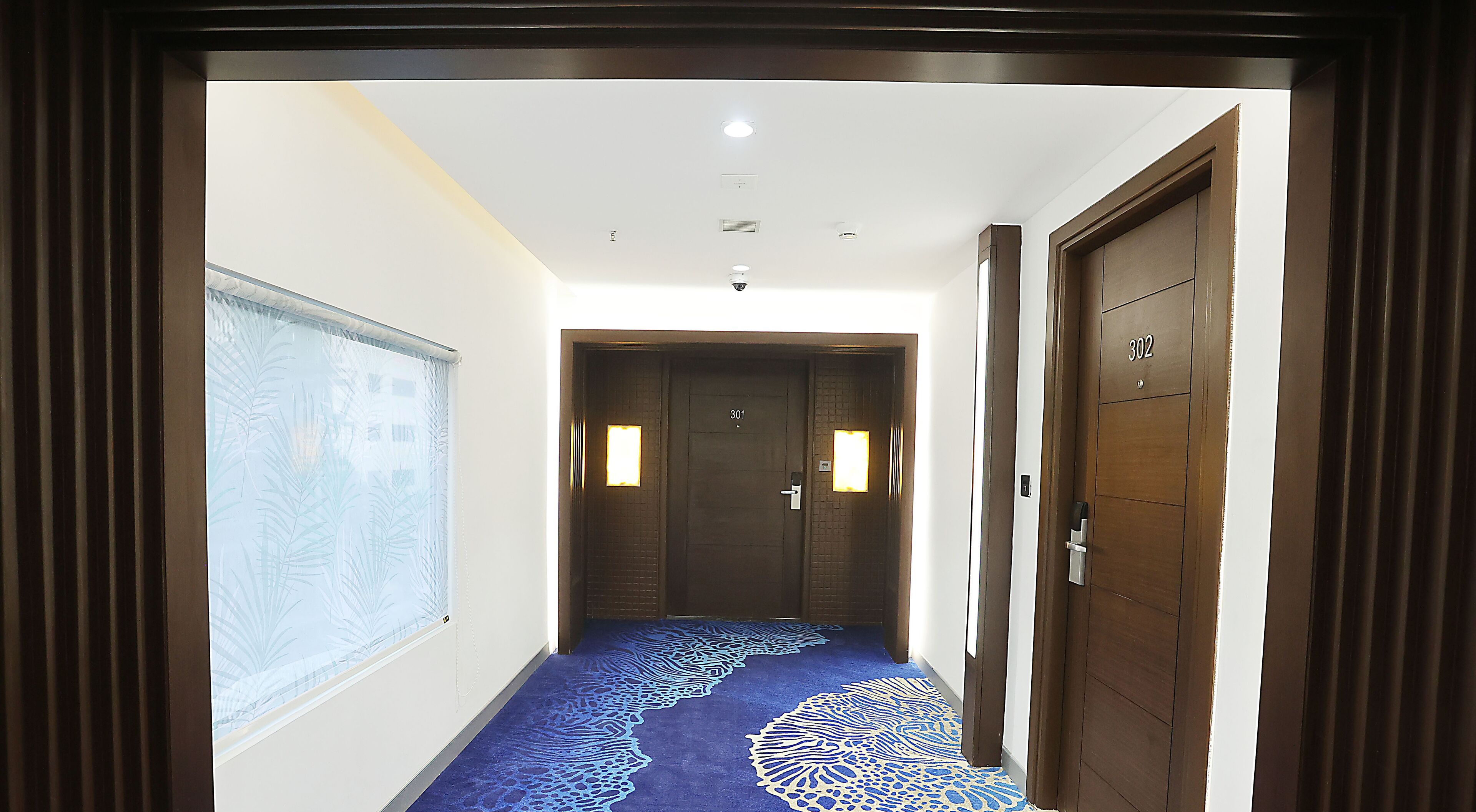 A hallway with patterned carpet, two doors with numbers, and a window with a view of palm trees.