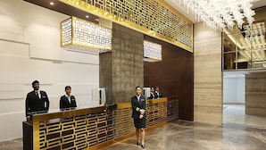 A reception area with a modern design, featuring a reception desk, a decorative wall with geometric patterns, and a chandelier. - Pharos Hotels (Chennai)
