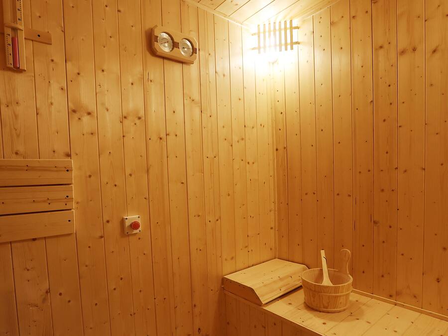 En bastu med träpanel, en träbänk, en väggmonterad värmare och en trähink med en öskar.