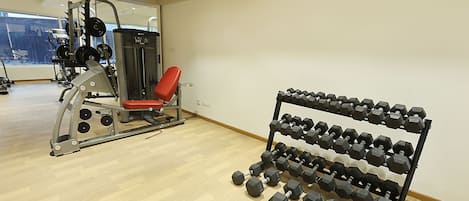 Un gimnasio con banco de pesas, estructura para sentadillas y estante con mancuernas.