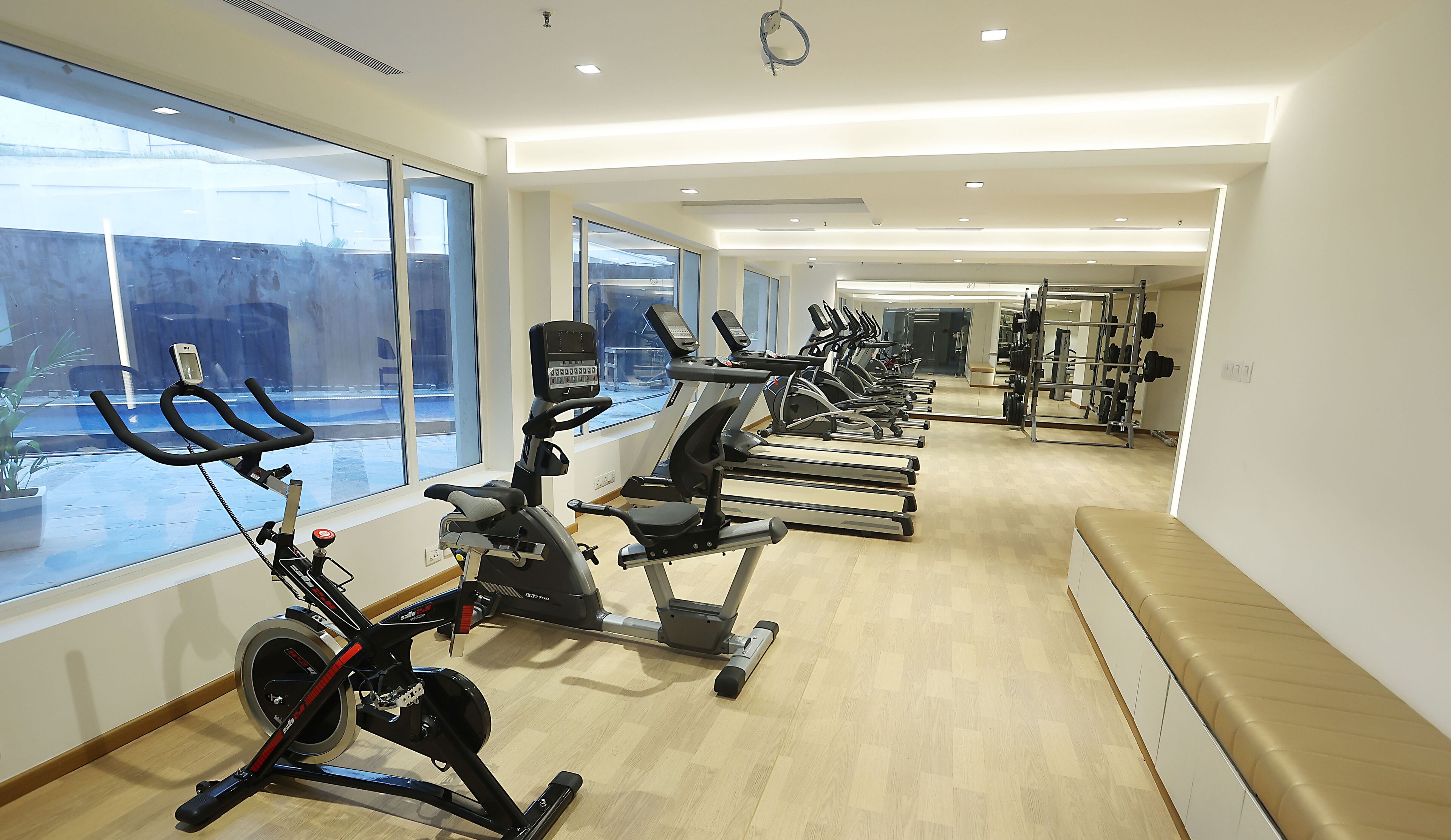 Un gimnasio con máquinas de cardio, equipo de levantamiento de pesas y amplios ventanales que ofrecen vistas al exterior.