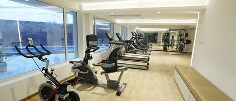 Un gimnasio con máquinas de cardio, equipo de levantamiento de pesas y amplios ventanales que ofrecen vistas al exterior.