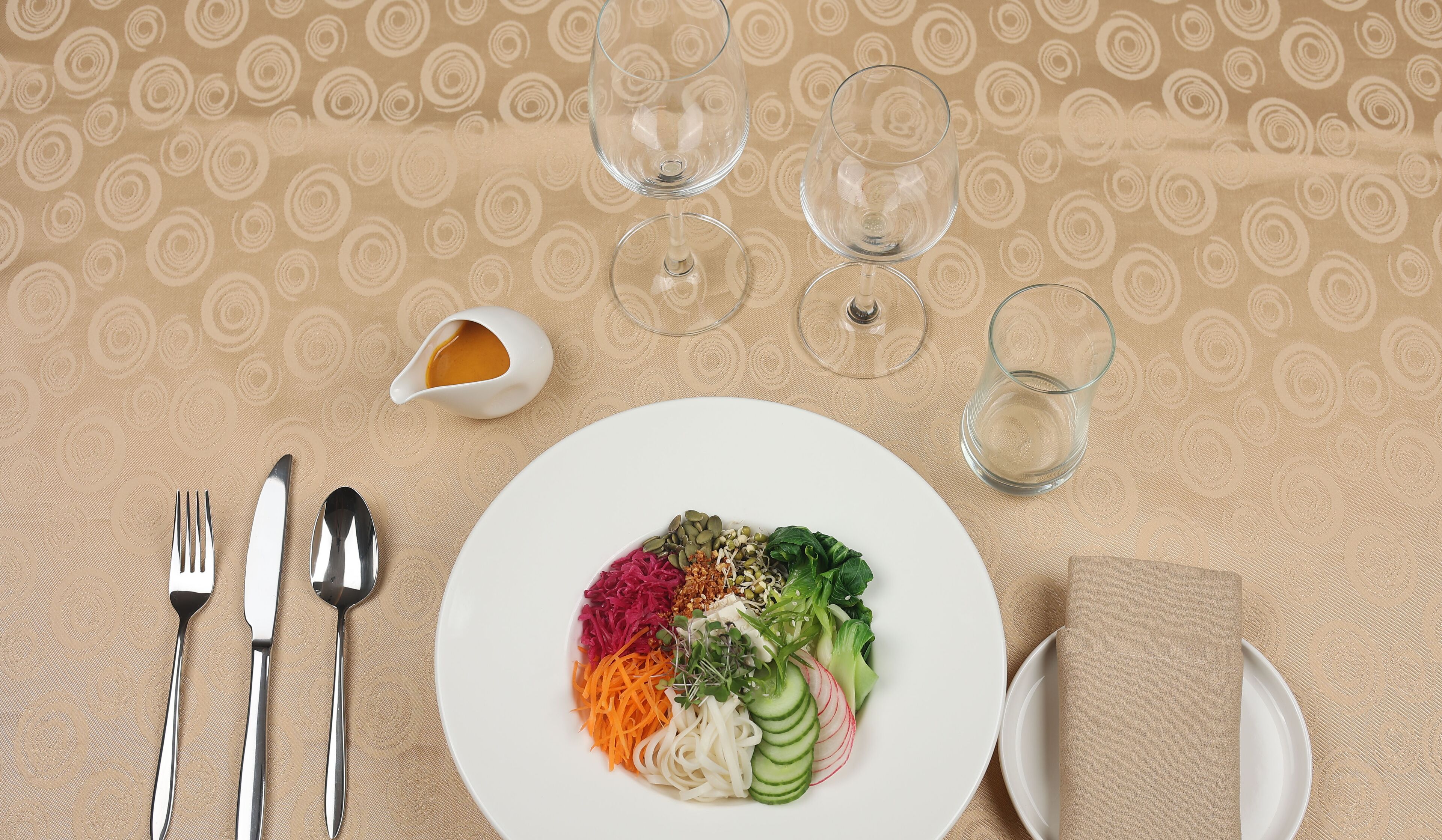 Una mesa dispuesta con un plato de verduras coloridas, un tazón pequeño de salsa y tres copas de vino.