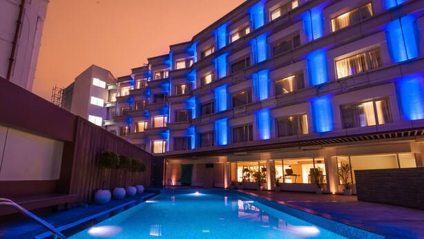 A swimming pool with a modern building in the background, featuring balconies and a well-lit facade. - Pharos Hotels (Chennai)