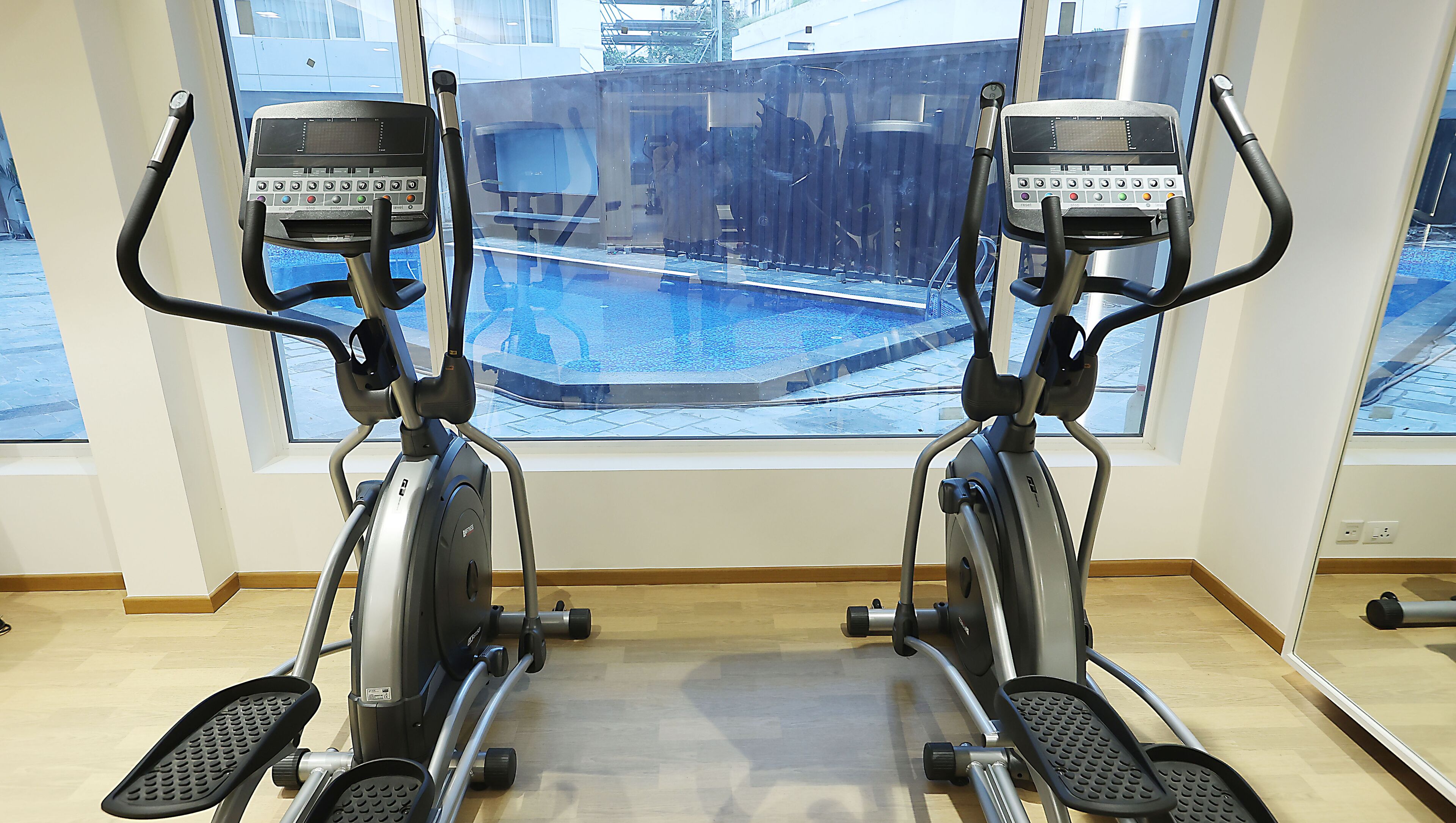Dos bicicletas estáticas en una sala con amplias ventanas que dan a una piscina.