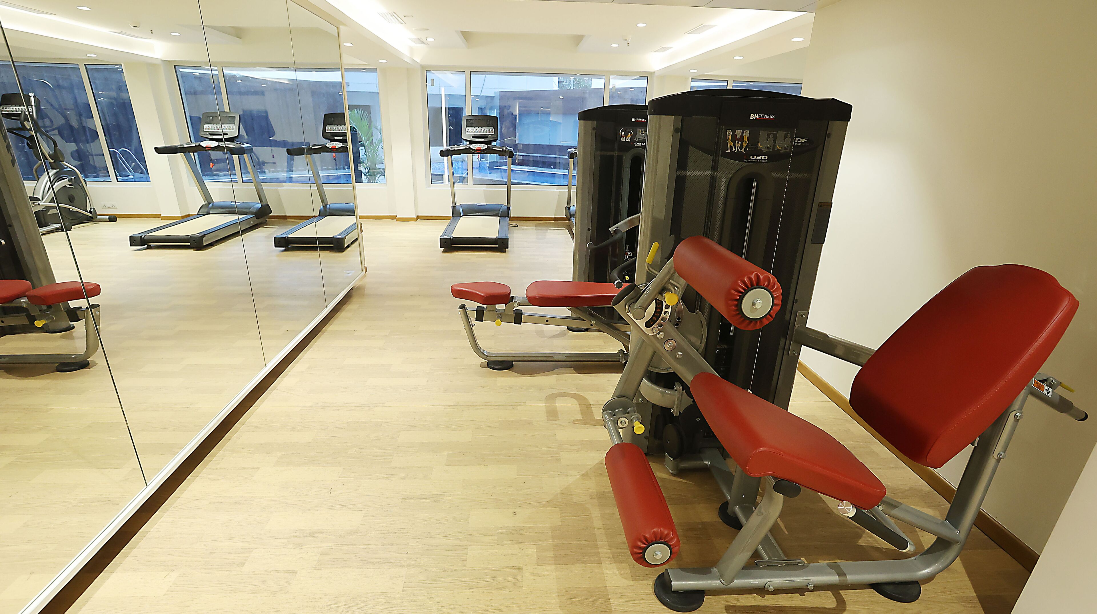 Een sportschool met cardioapparatuur, gewichten en een spiegelwand.