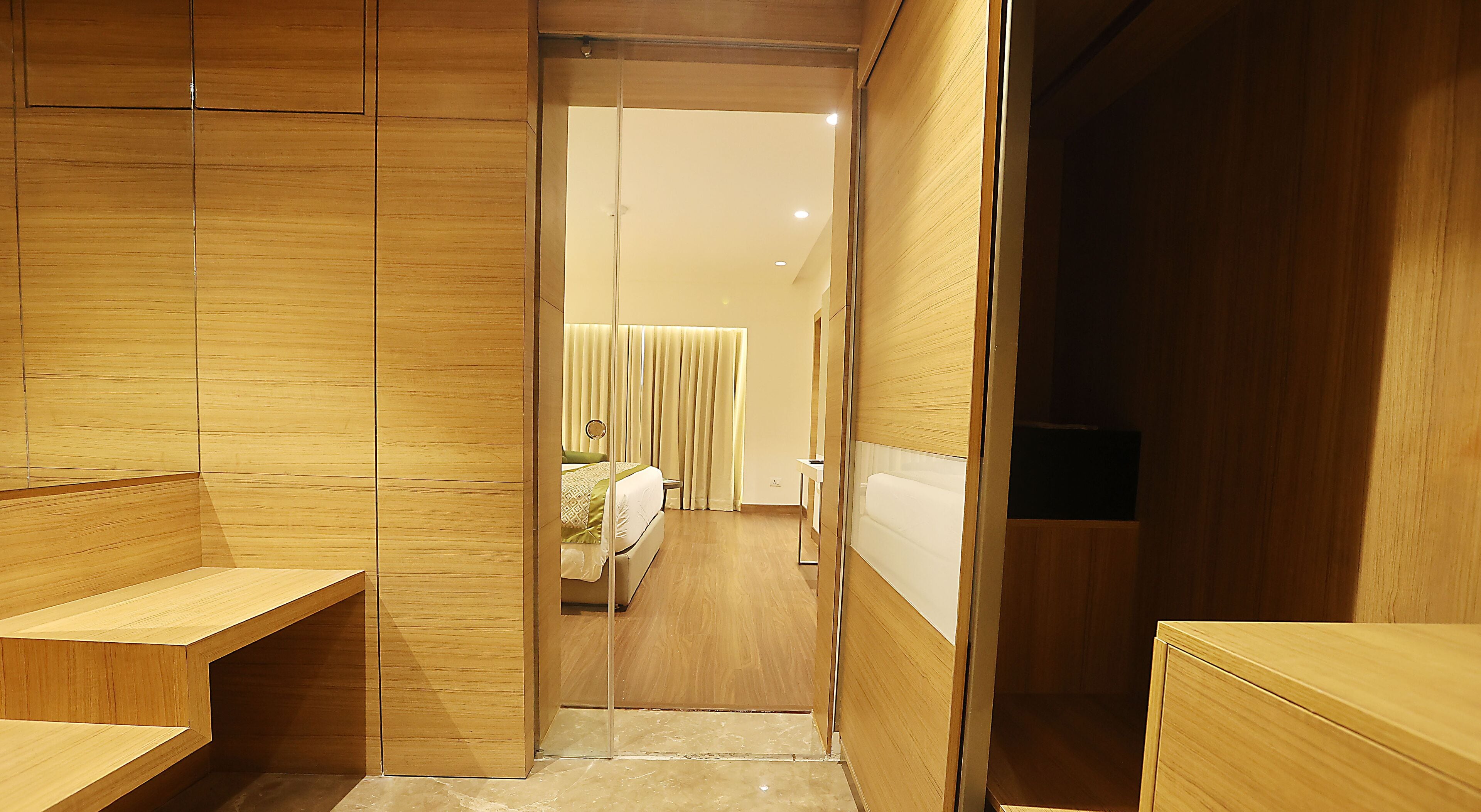 Una habitación de hotel moderna con un armario de madera, una mesita de noche y una cama con una manta verde.