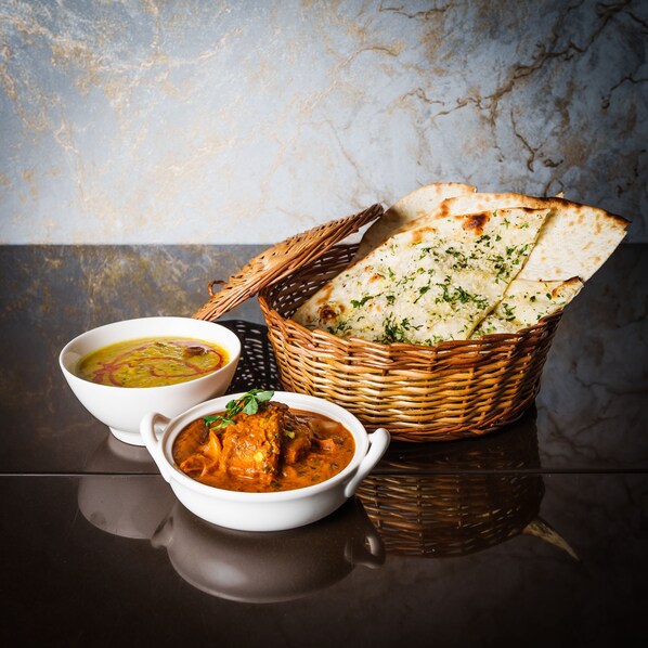 A dining table with two bowls of soup and a basket of flatbread. - Pharos Hotels (Chennai)