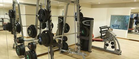 Un gimnasio con equipo de levantamiento de pesas, incluyendo una estructura para sentadillas y diferentes pesas.