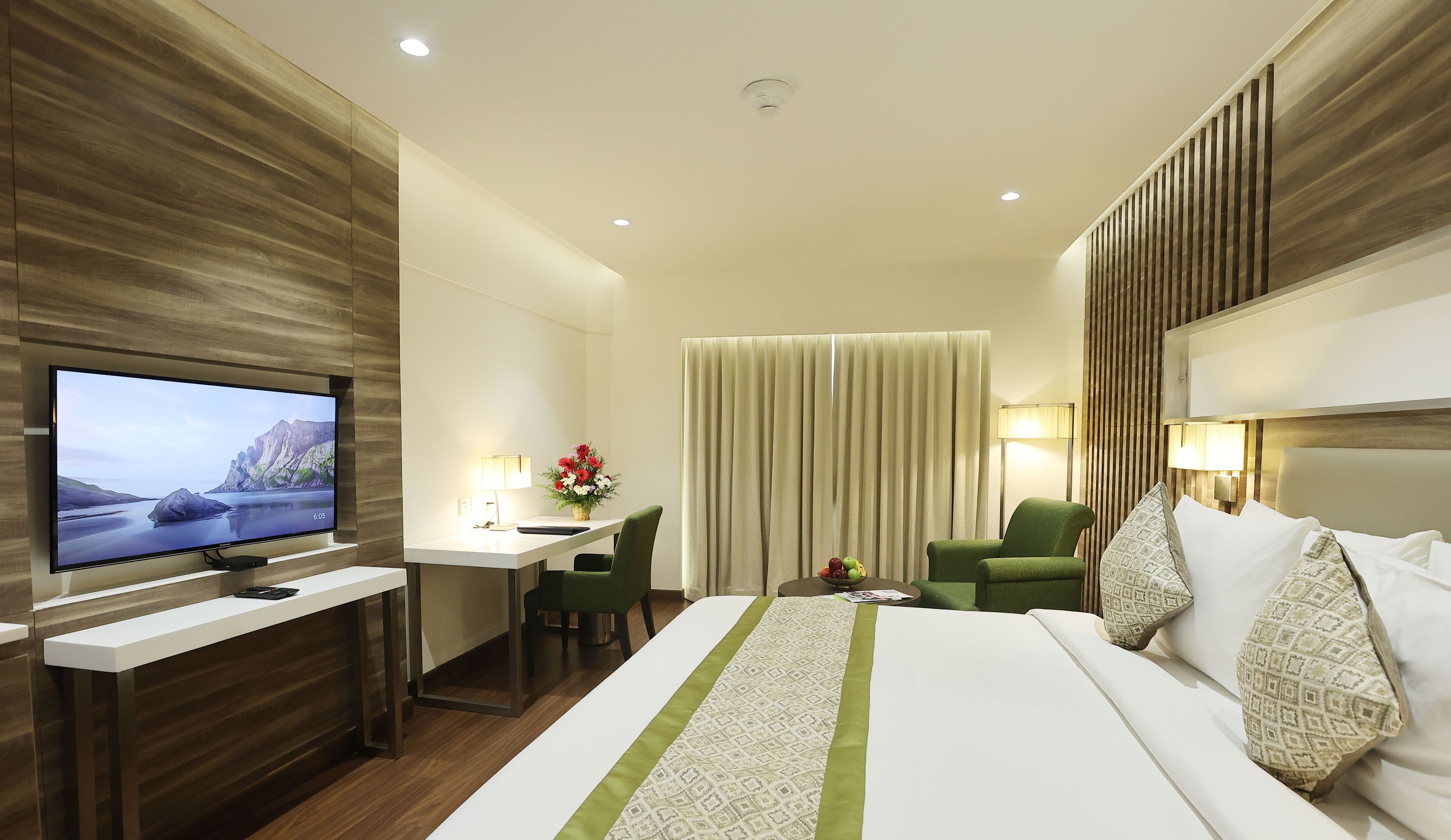 Una habitación de hotel con una cama grande, un escritorio con silla, un televisor y una ventana con cortinas.