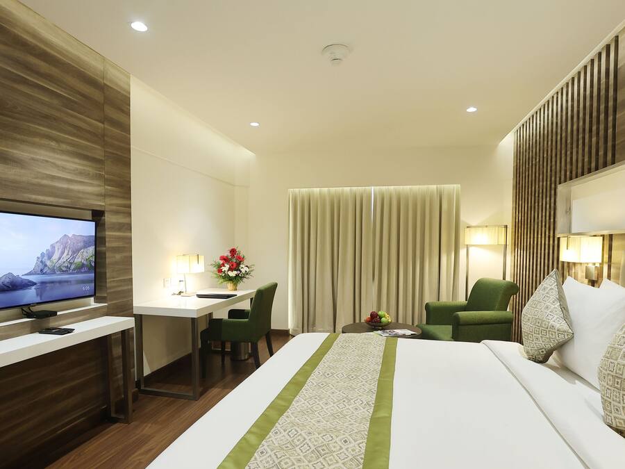 Una habitación de hotel con una cama grande, un escritorio con silla, un televisor y una ventana con cortinas.
