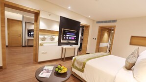 A hotel room with a bed, a desk, a television, and a fruit bowl on the coffee table. - Pharos Hotels (Chennai)