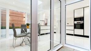 Eine moderne Küche mit Edelstahlgeräten, eine Glastür zu einem Essbereich mit Tisch und Stühlen sowie ein Blick ins Freie.