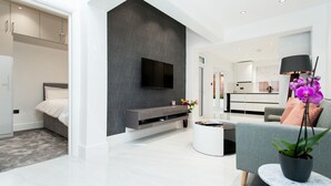 Ein modernes Wohnzimmer mit grauem Sofa, einem flachbildfernseher an einer grauen Wand, einem kleinen Couchtisch und einer Topfpflanze.