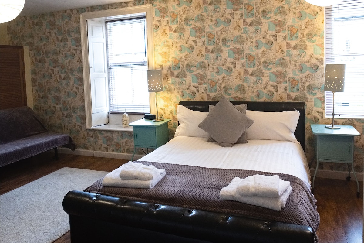 A bedroom with a bed, bedside tables, a window, and a patterned wall.