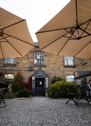 A stone building with a dark entrance door, beige umbrellas, and gravel ground. - LABURNUM HOUSE & BISTRO EN GLAZE (Wylam)