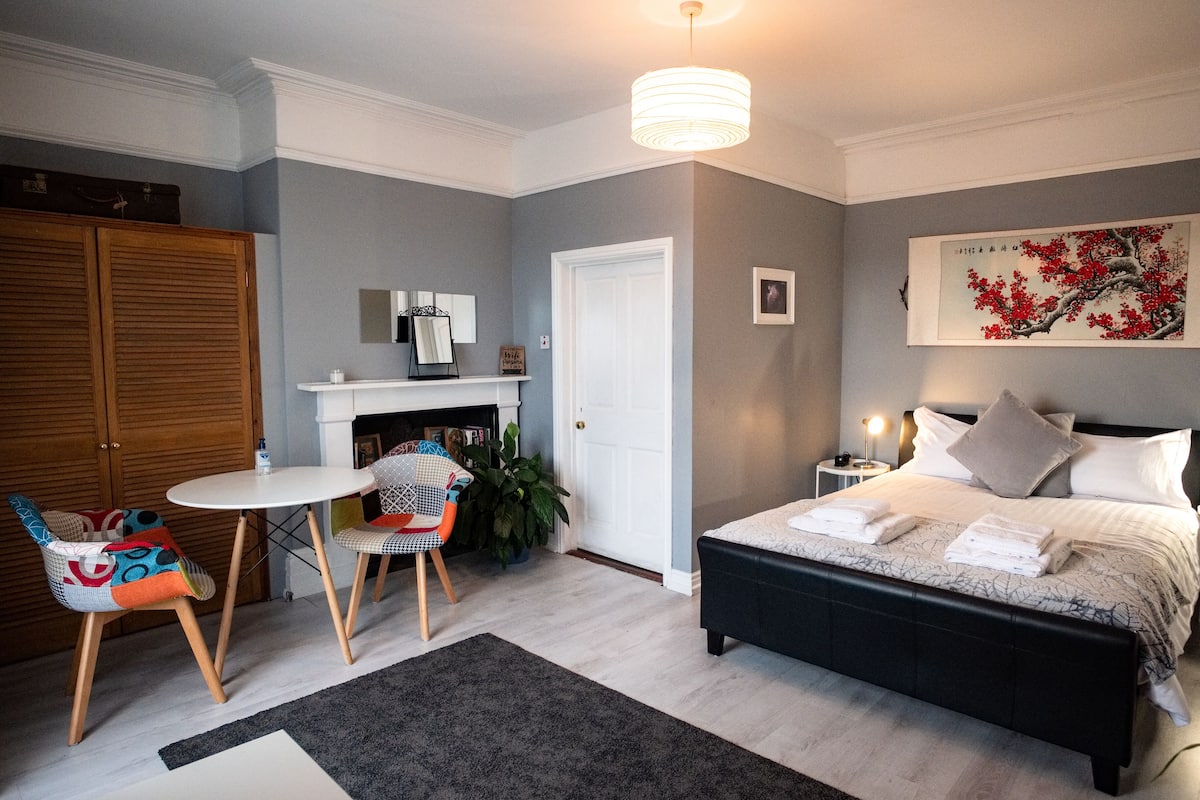 A bedroom with a bed, a chair, a table, a wardrobe, and a fireplace.