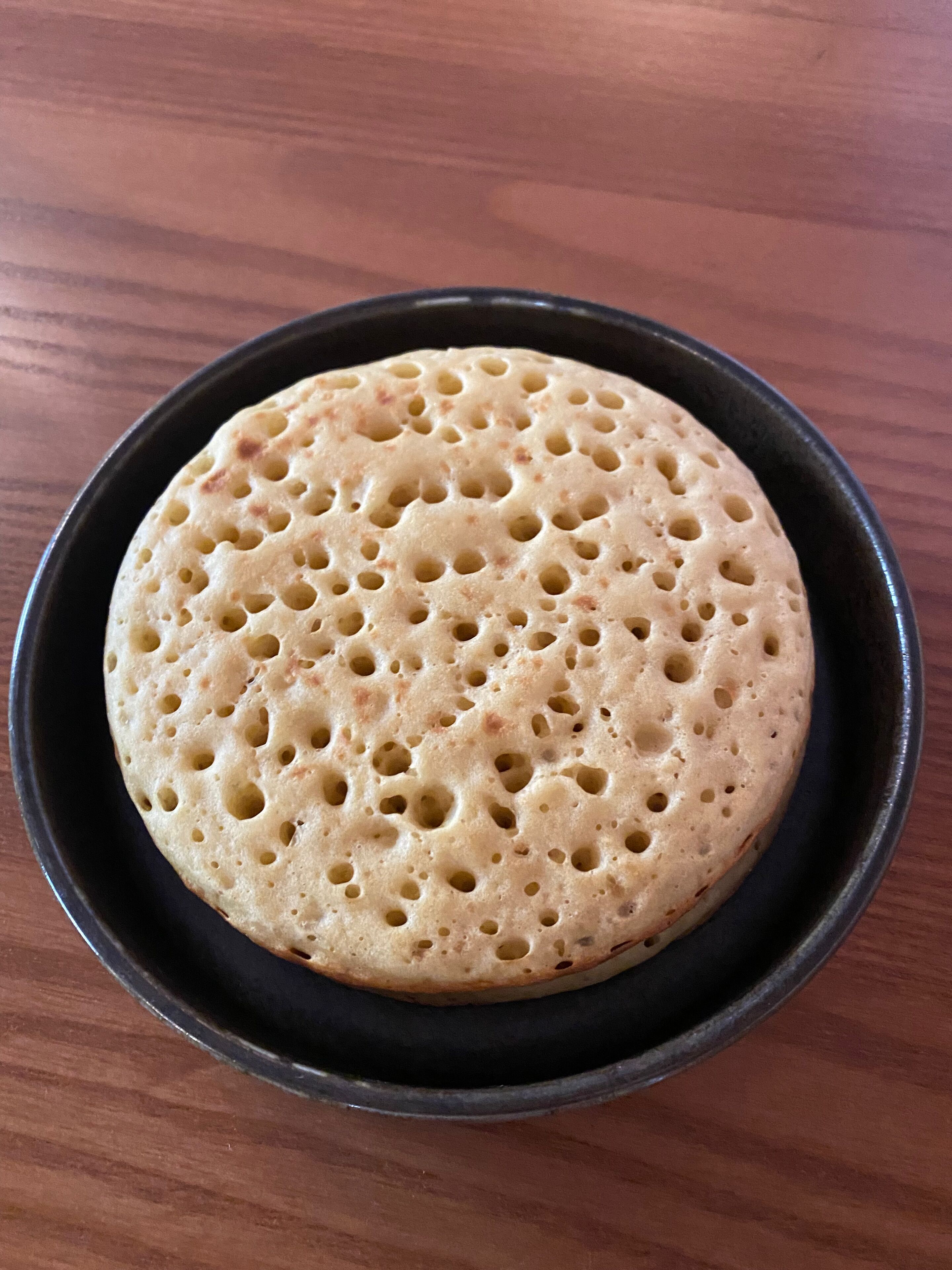 A round, flat, perforated bread on a black plate.