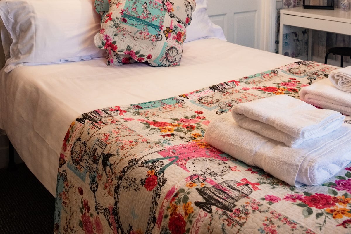 A neatly made bed with floral bedding, a framed picture above, and a bedside table with a lamp.