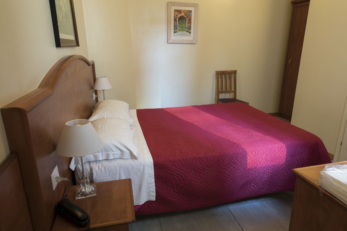 A neatly made bed with a red blanket, a bedside lamp, and a wooden nightstand.