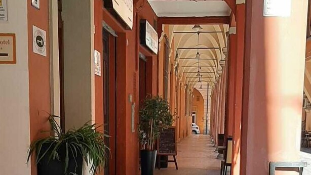 A covered walkway with stone flooring, potted plants, and signs indicating hotel rooms. - BuonHotel Bologna Centro (Bologna)