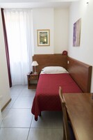 Een hotelkamer met een houten bed, nachtkastje, tafel, stoel, een schilderij aan de muur en een raam met gordijnen.