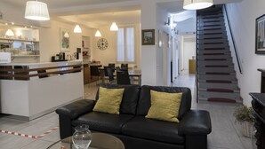 A modern living room with a black leather sofa, a glass coffee table, and pendant lighting. A kitchen area with a bar counter and dining table is visible in the background. - BuonHotel Bologna Centro (Bologna)
