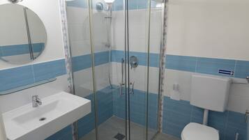 Un baño con ducha envuelta en vidrio, lavamanos, inodoro y espejo.