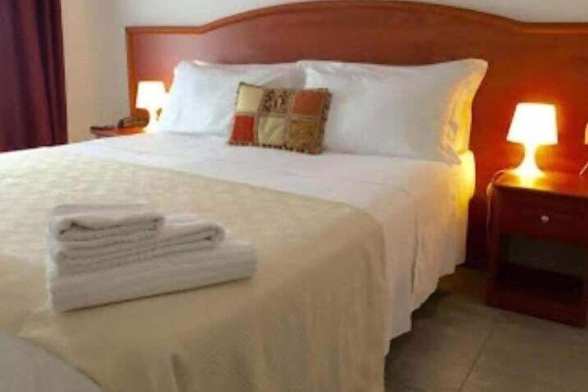 A neatly made bed with white linens, a folded towel, and a wooden headboard.