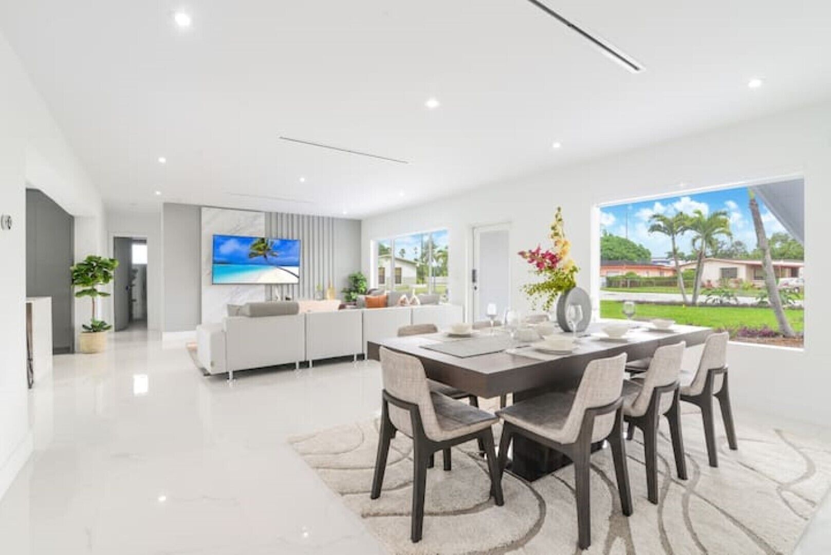 A modern kitchen with a dining area, large windows, and a view of the outdoors.