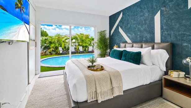 Ein Schlafzimmer mit einem großen Bett, Blick auf einen Swimmingpool und einer blauen Akzentwand.