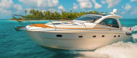 A white speedboat on water with a clear sky and distant green land.