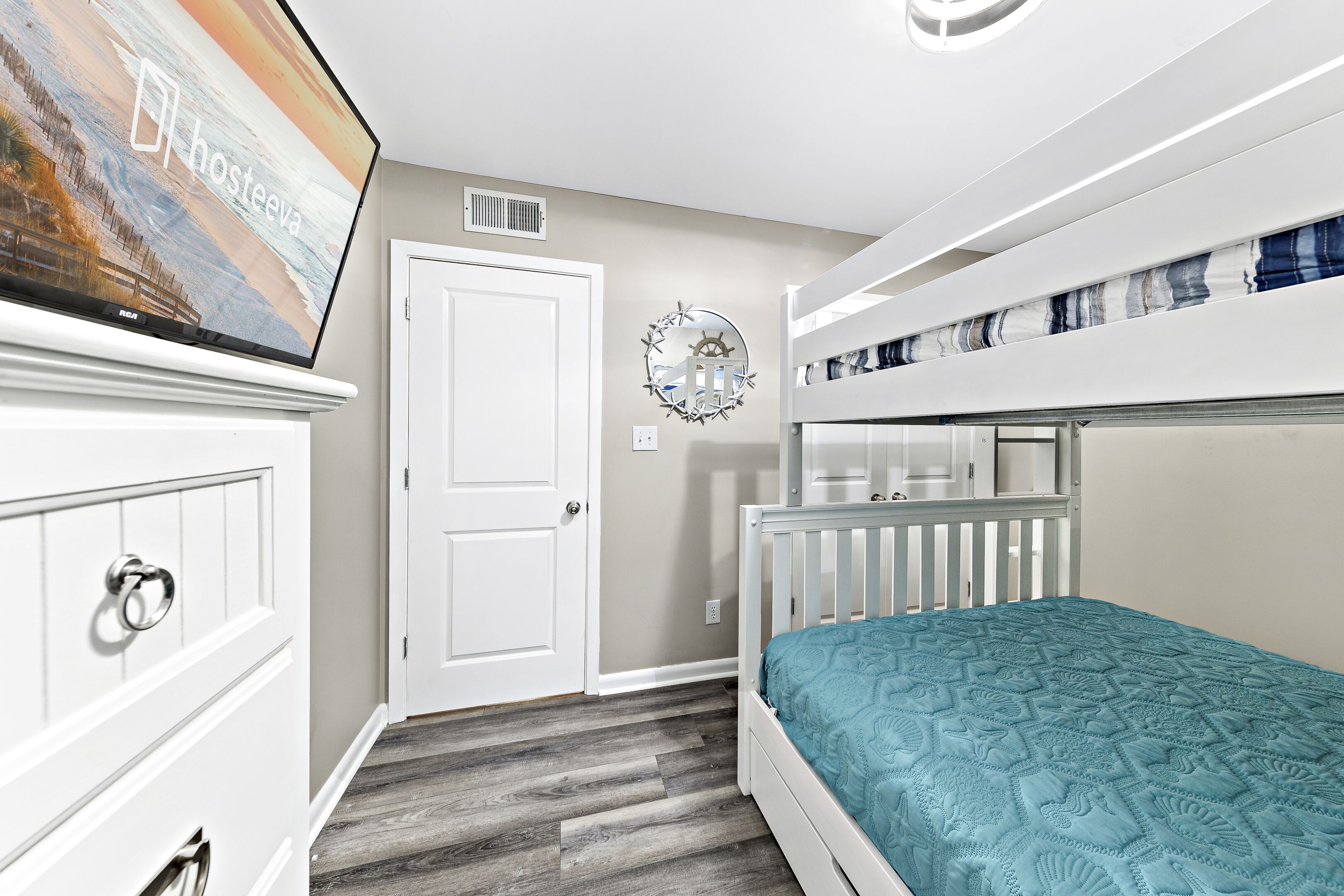 Une chambre avec un lit superposé, une commode, un téléviseur et une horloge murale.