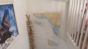 A staircase with a wooden handrail, a map on the wall, and a painting of a ship. - Fisherman's cottage (Île-d'Arz)